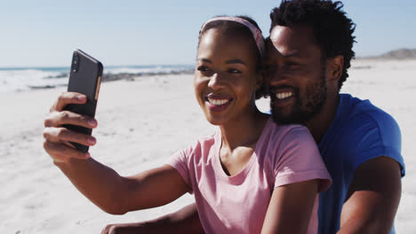 African-american-couple-smiling-taking-selfie-with-smartphone-on-the-beach