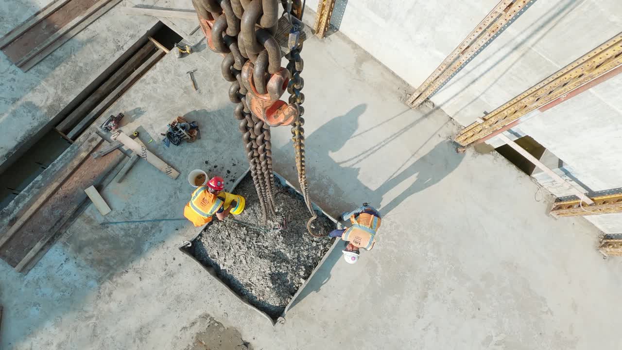 POV top down, construction workers connecting tower crane chains to container full of gravel at a construction site