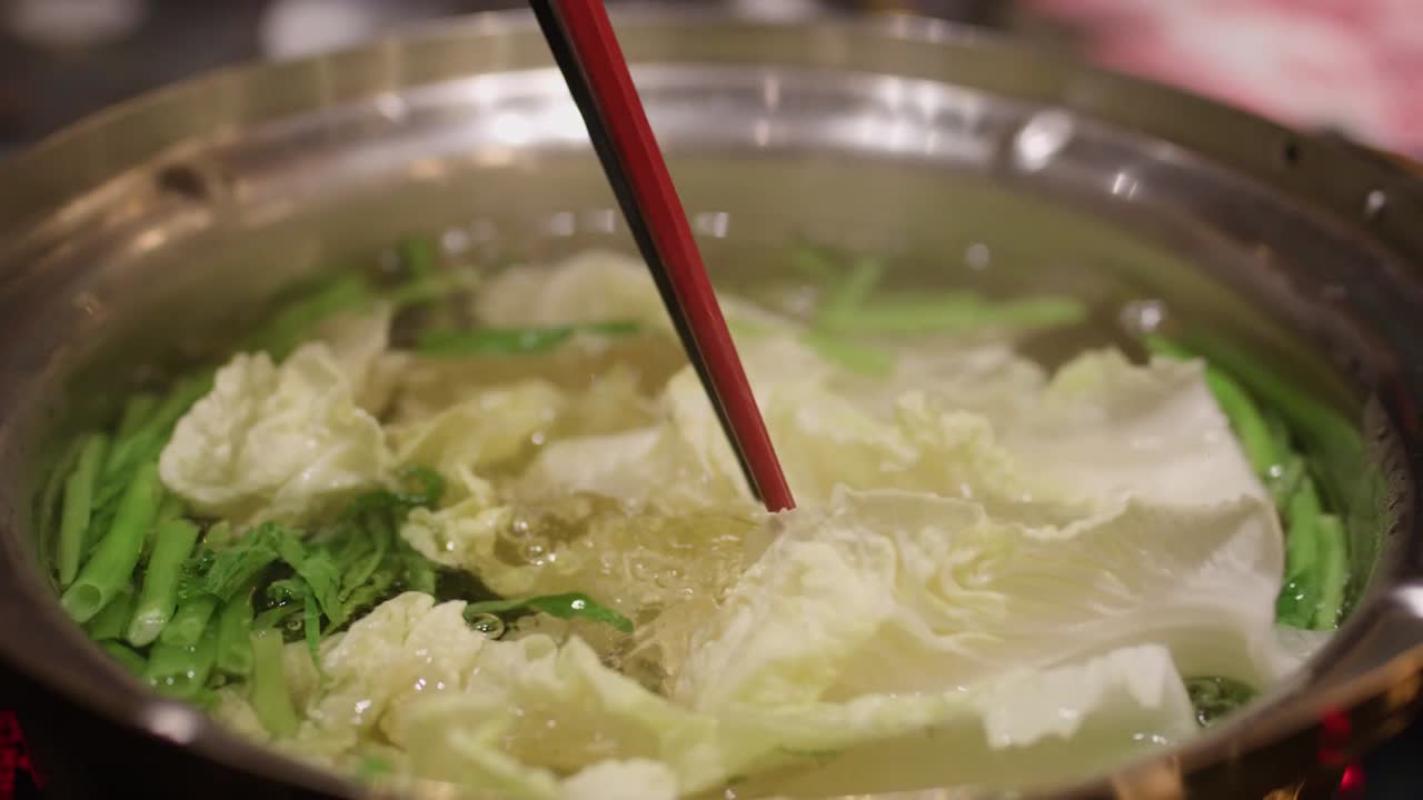 Cận cảnh cải thảo được thêm vào nồi kim loại đang sôi chứa đầy rau xanh.