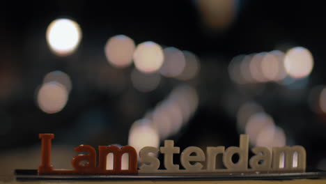 view of small plastic figure of iamsterdam letters sculpture on the bridge against blurred cityscape amsterdam netherlands