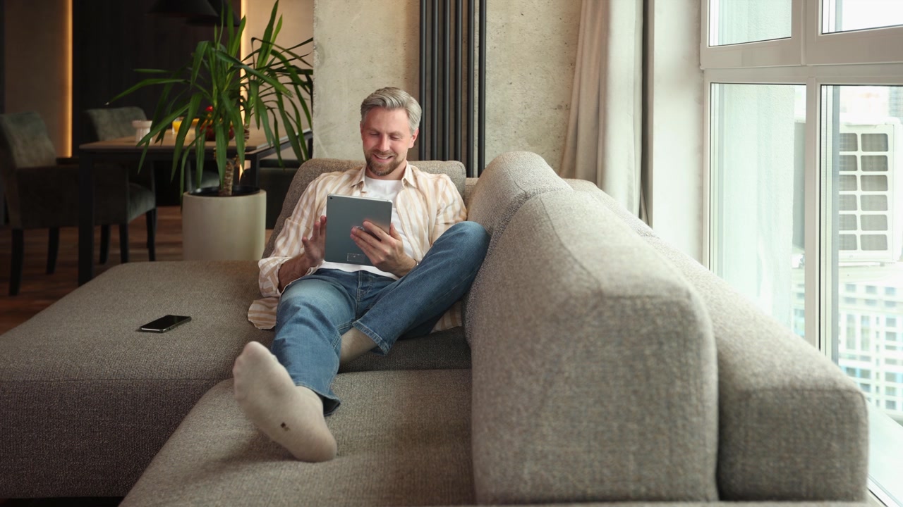 Uomo felice che si rilassa sul divano e usa il tablet digitale a casa