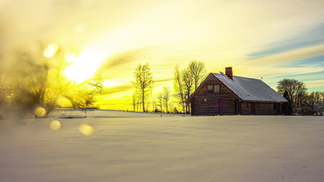 timelapse shot of sun setting in the background over snow covered landscape alongside a wooden cottage during evening time