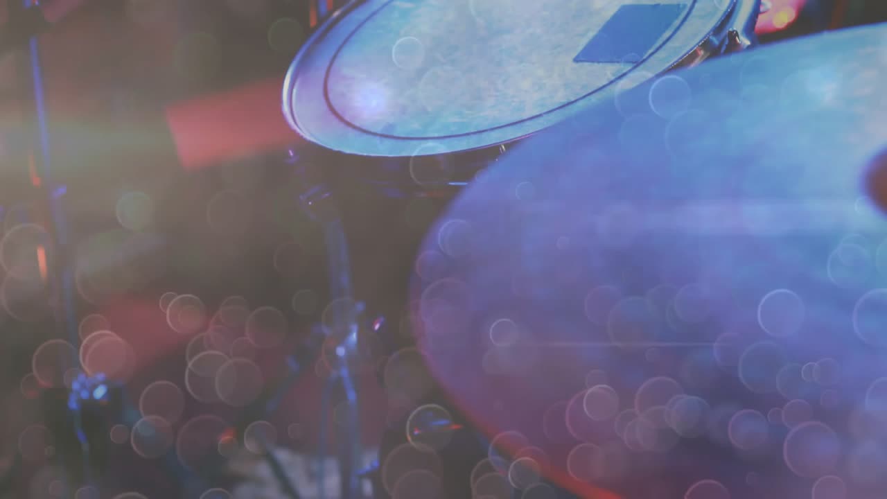 La telecamera si sofferma sul piatto con un bokeh rosso fluttuante che si sposta sulla pelle del rullante mentre una bacchetta rossa colpisce.