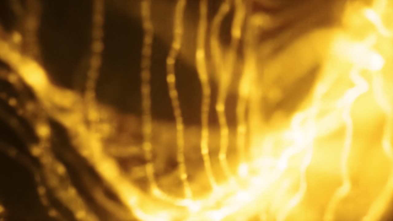 The visual captures dynamic golden patterns streaming through a dark environment, showcasing the interplay of light and shadows in an artistic manner. The movement creates an engaging atmosphere.