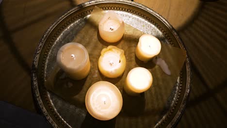 the shot of light candles on a metal tray on a wooden table in a cozy home in the dark evening