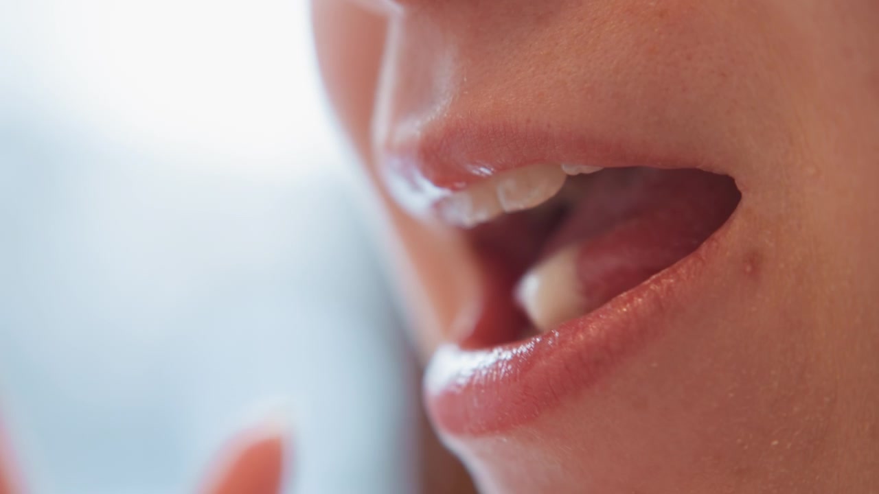 Extremnahe Ansicht des unteren Gesichts, das Lippen, Kinn und zarte Hautdetails zeigt, während eine Person ein cremiges Dessert kostet, einen leichten Rückstand auf der Oberlippe hinterlässt und unter sanftem Innenlicht in ein entspanntes Lächeln übergeht