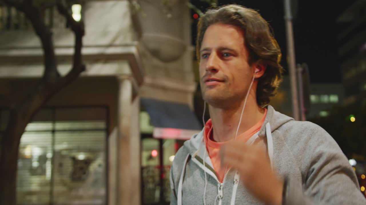 하 ⁇ 색 남성이 스포츠를 하고, 웃으며, 저녁에 거리에서 이어폰을 착용하고 있습니다.