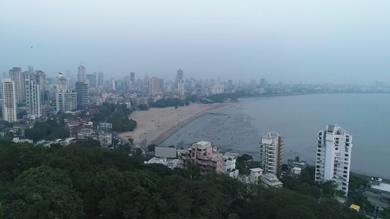 Una ripresa cinematografica con drone del famoso punto panoramico Marine Drive Chaupati Beach nella regione di South Bombay della città di Mumbai, con vista sulla collina dei giardini pensili e la foresta, in un movimento lento e fluido.