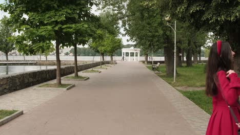 Hermosa-Morena-En-Rojo-Camina-En-El-Parque-Cerca-Del-Lago