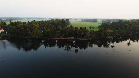 reflections on lagoon with rural fields near alleppey town in kerala, india