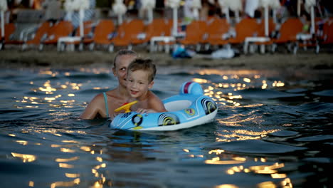 hijo con anillo de goma y madre bañándose en el mar