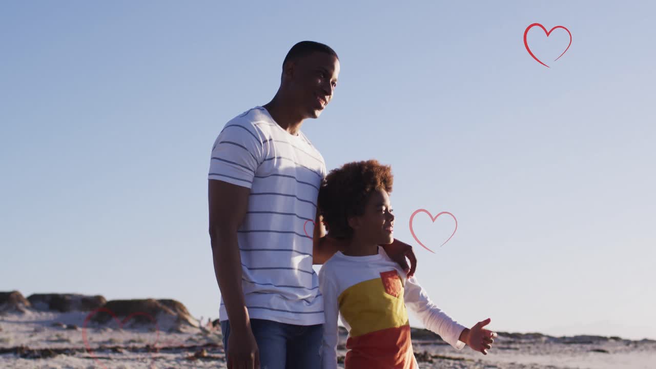 Animazione di cuori sopra un padre e figlio afroamericani in piedi sulla spiaggia al tramonto