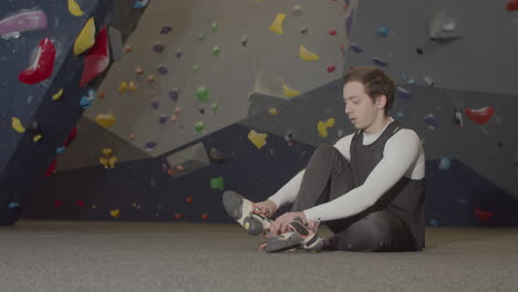 young male athlete sitting in bouldering gym and putting climbing shoes on