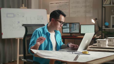 asian man engineer looking at blueprint and typing on a laptop at the office