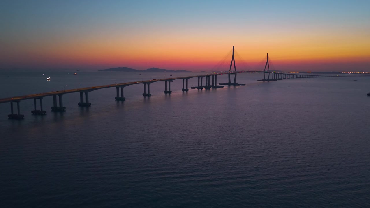 Vista aerea si avvicina al Ponte di Incheon all'ora blu mentre il traffico illuminato attraversa le torri strallate sotto un cielo vibrante al tramonto