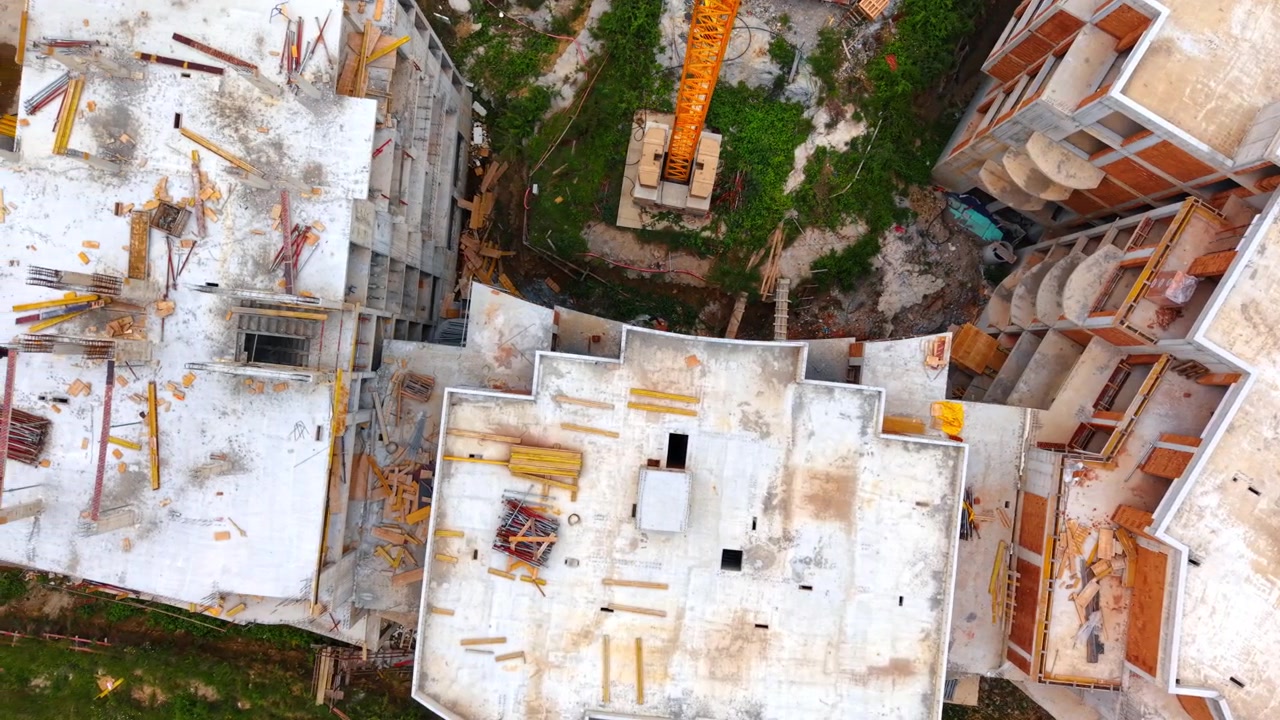 Vista superior de edificio residencial de hormigón en construcción con grúa. Vista aérea cenital de tejados de edificios de hormigón sin terminar y una base de grúa torre amarilla en la obra
