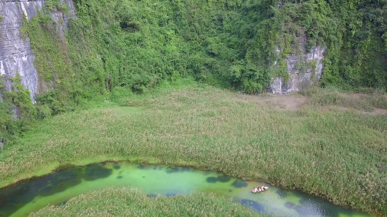 Cinematic drone footage of majestic green limestone peaks. Canoeing among ricefields in the wild jungle in the spring with boat tour canal in Trang An, Ninh Binh, Vietnam