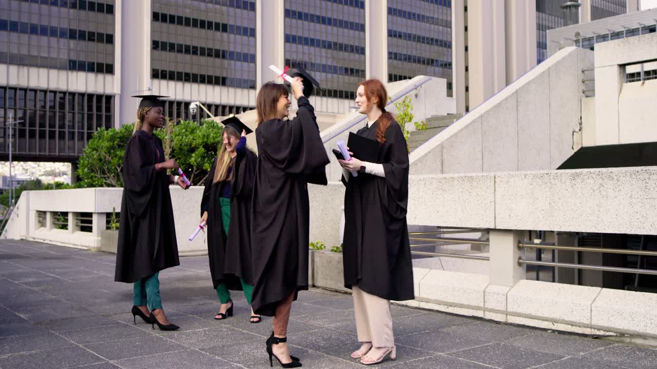 Donne di etnie diverse in toga dopo la cerimonia in piazza, una rossa che si scatta un selfie con il telefono, con diplomi e spazio per il testo.