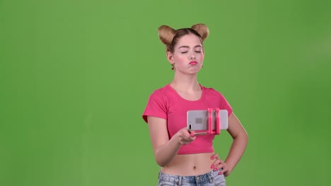 a young woman poses for selfies with a smartphone on a selfie stick against a green screen