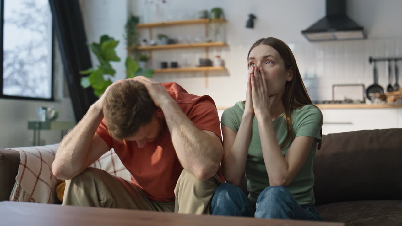 Shocked couple cheering sport game on TV at home closeup. Disappointed fans