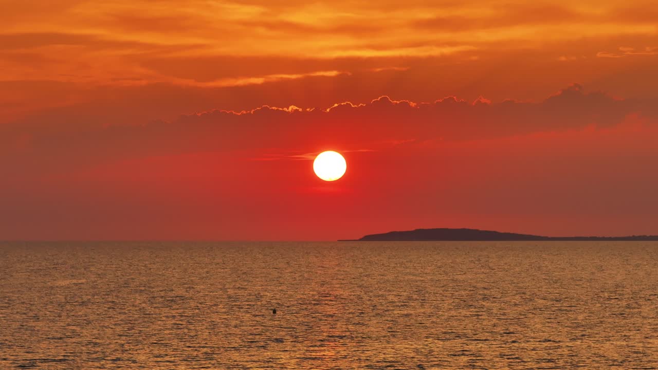 Watch the sky glow in golden hues as the sun sets over the ocean, captured from above. This aerial footage reveals the peaceful beauty of the coastline at dusk, with the waves softly hitting the shore