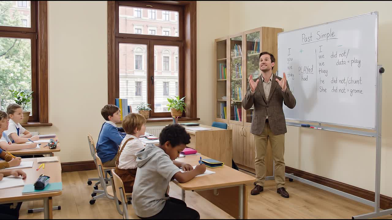 Učitel vysvětluje minulý čas prostý na tabuli, zatímco si studenti píší poznámky v učebně.