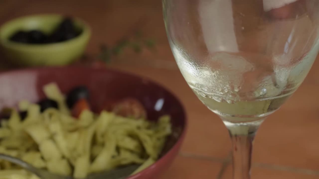 White wine pouring into glass with pasta lunch background close up