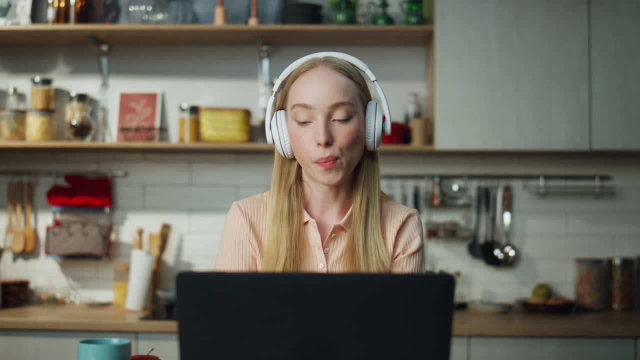 Online student listening music by headphones at kitchen with laptop close up.