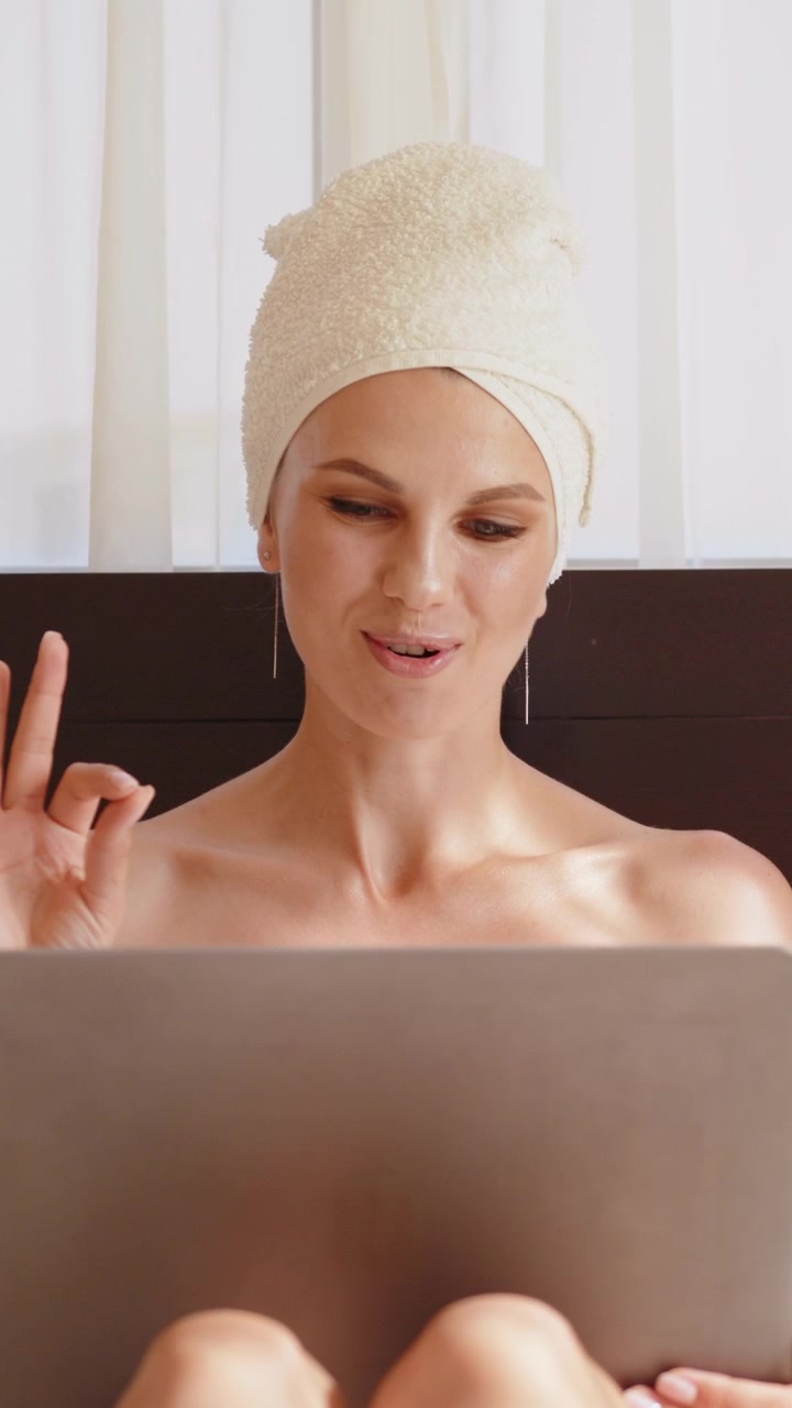 Una donna con un asciugamano in testa sorride mentre guarda lo schermo di un laptop.