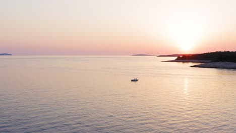 Serene-View-Of-Lone-Boat-Sailing-Across-The-Vast-Ocean-Surrounding-The-Losinj-Island-With-Pink-Sky-Sunset---Wide-Shot