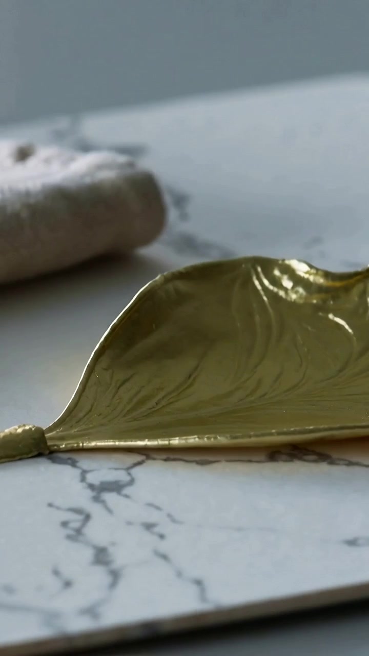 Video verticale: Telecamera in movimento che rivela un oggetto in foglia d'oro su un pannello di marmo, mostrando texture e lucentezza.