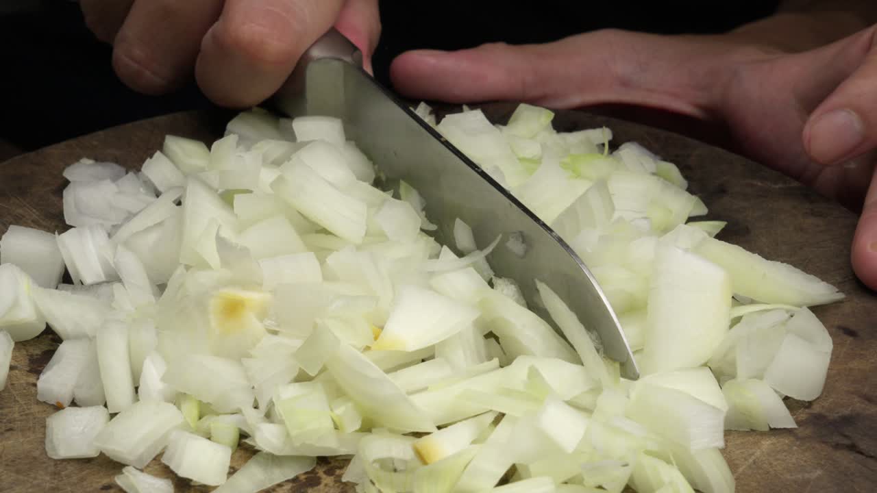 Close-up of knife chopping onion into small pieces on wooden board