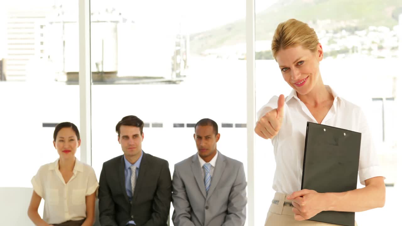 Businesswoman giving thumbs to camera in front of applicants