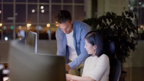 diverse male and female colleague talking and using computers at night in office