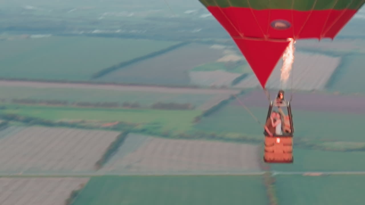 couples flying in hot air balloon over patchwork farmland at sunset as pilot fires burner for ascent capturing romantic aerial journey over vast green fields with smiling travelers panoramic view