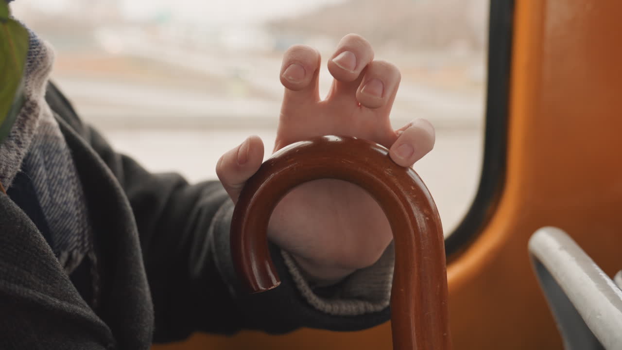 Un individuo regola un bastone da passeggio in legno. Una persona apporta modifiche a un classico bastone di legno vicino al finestrino dell'autobus, personalizzando attentamente il proprio bastone da passeggio vintage.