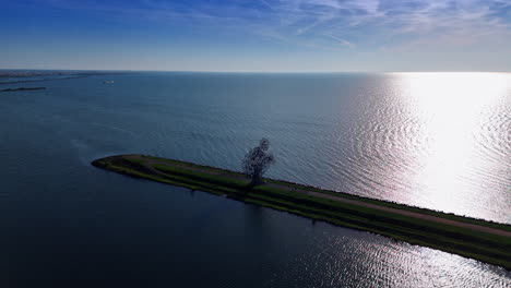 Approaching the metal sculpture of a squatting man on the dam of the Merkemeer Lake. Sun reflects on the surface of the lake. Aerial view. Lelystad, The Netherlands.