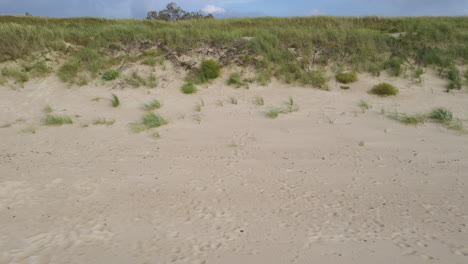 aerial: panning shot of hill covered with beach sand and grass with blue sky