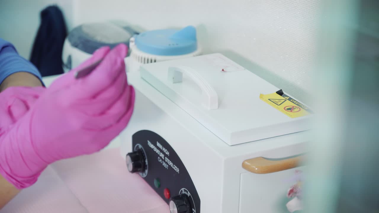 A beautician with gloves takes out tools from a temperature sterilizer