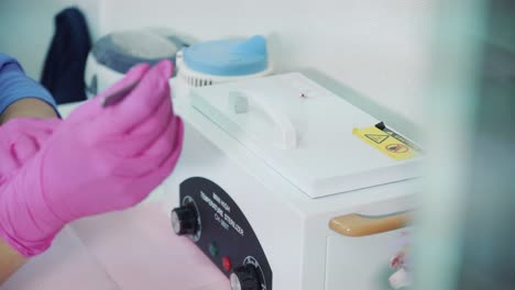 a beautician with gloves takes out tools from a temperature sterilizer
