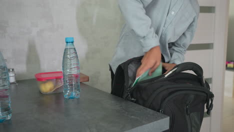 girl and boy in casual wear packing backpacks on kitchen counter placing notebooks water bottles lunch boxes and folders into bags preparing school day with sibling teamwork and organization