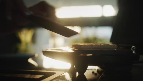 woman prepares a hot sandwich for breakfast. from the window the sun shines on an electric sandwich maker