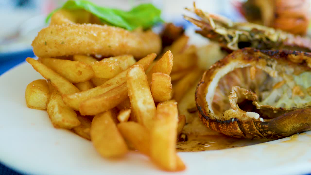 Rotating close-up of grilled shellfish, fried seafood, and fries on a white plate, daylight