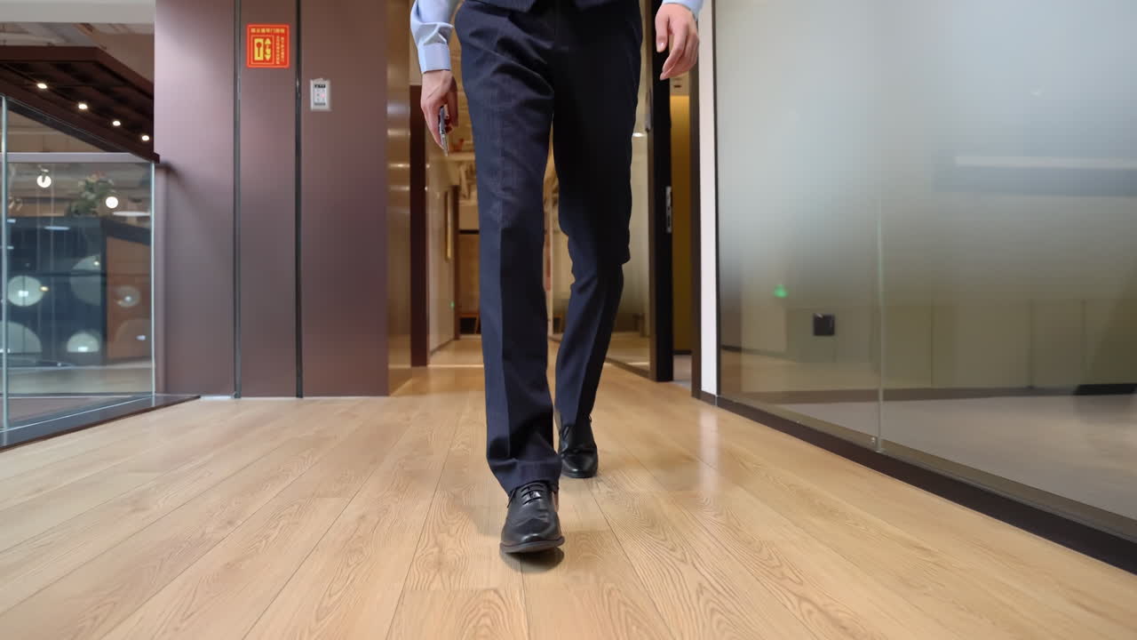 Confident businessman in a formal suit walks down modern office hallway towards camera, spacious office corridor with glass windows, symbolizing corporate professionalism and business environment