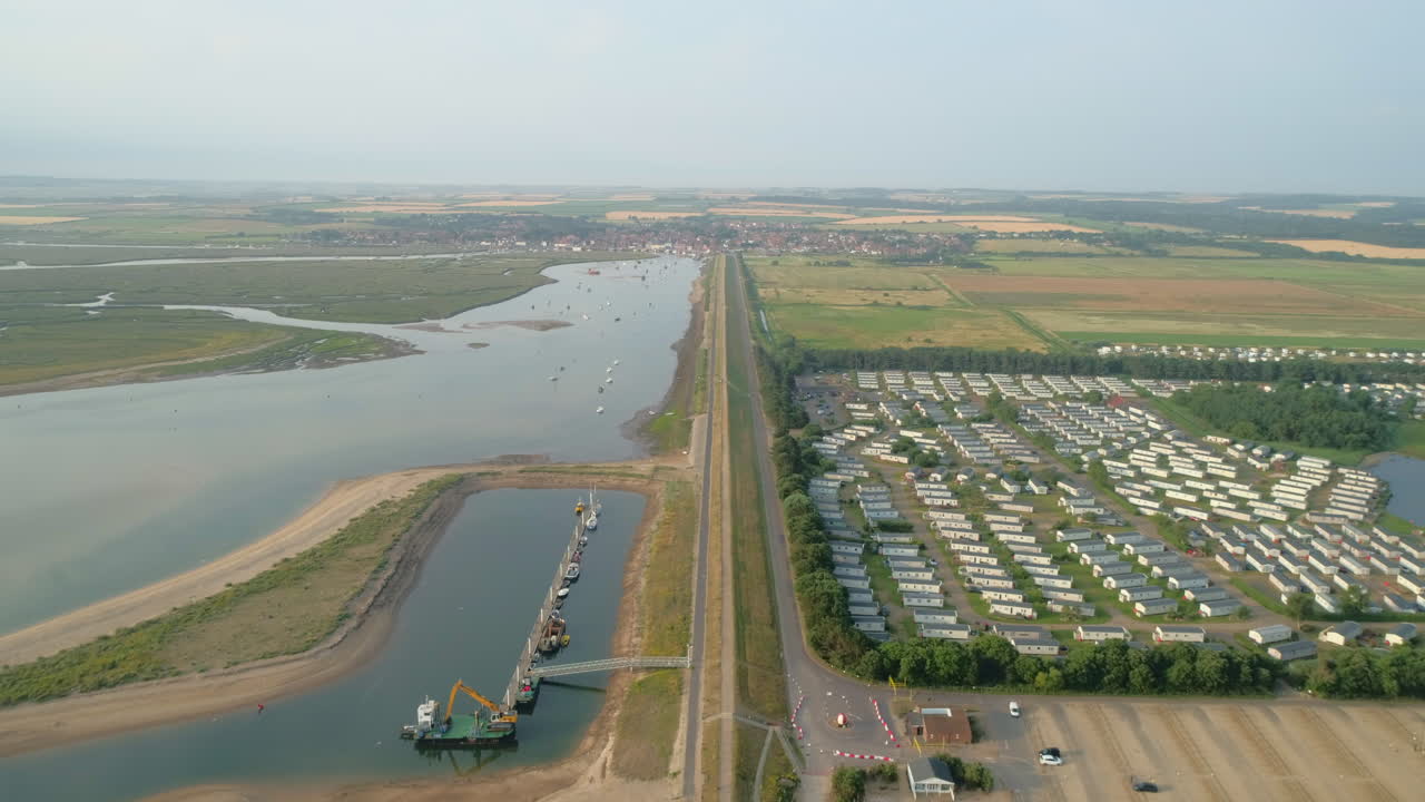 만조 때 개울과 정적인 캐러밴 휴가용 주택 공원이 있는 바다 옆의 우물을 돌아보며 선을 긋는 높은 드론