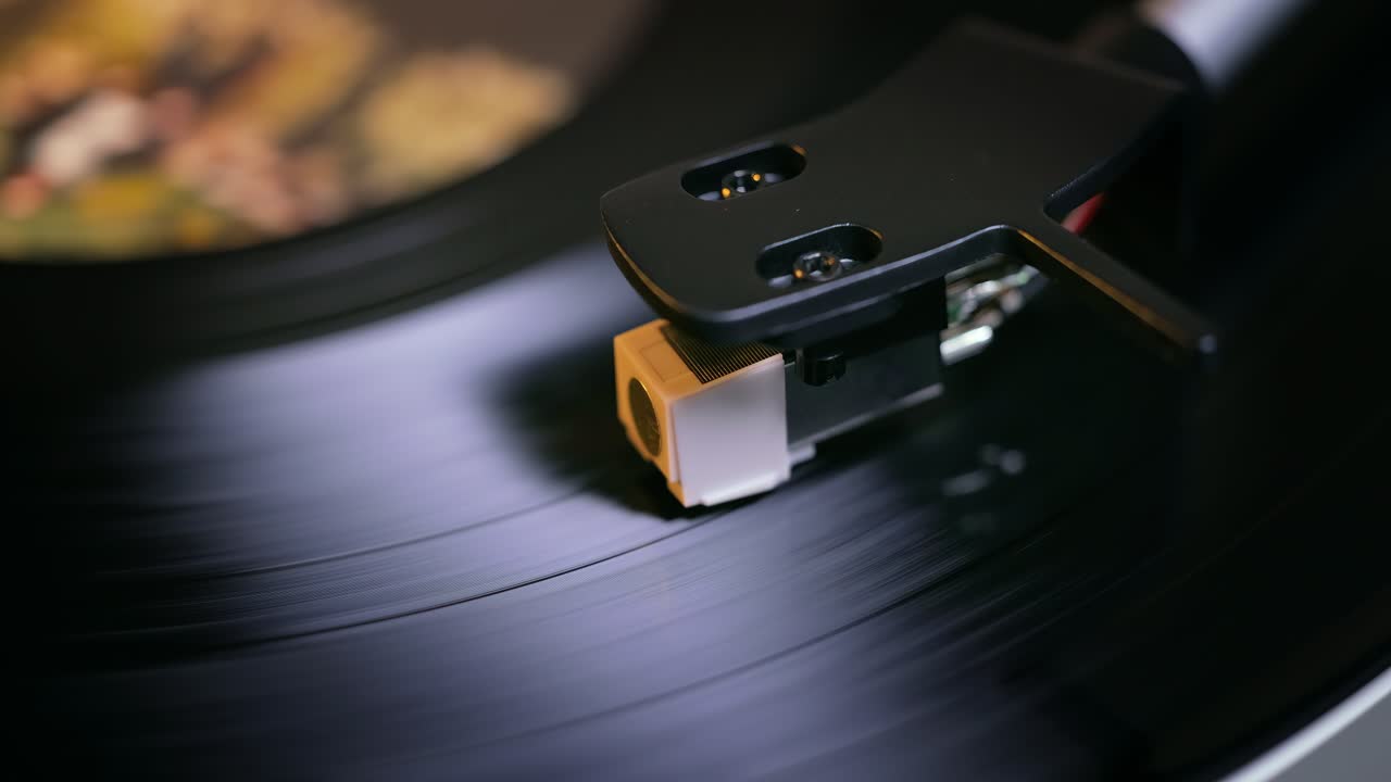 Primo piano dettagliato del braccio di un giradischi con testina bianca, posizionato su un disco in vinile nero sul piatto, che evidenzia la precisione delle apparecchiature audio