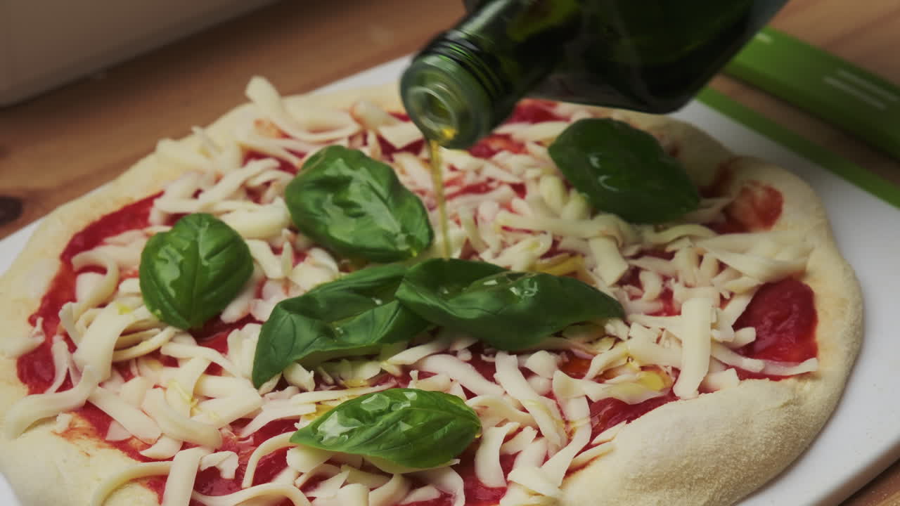 Close-up of drizzling golden olive oil over a freshly assembled margarita pizza