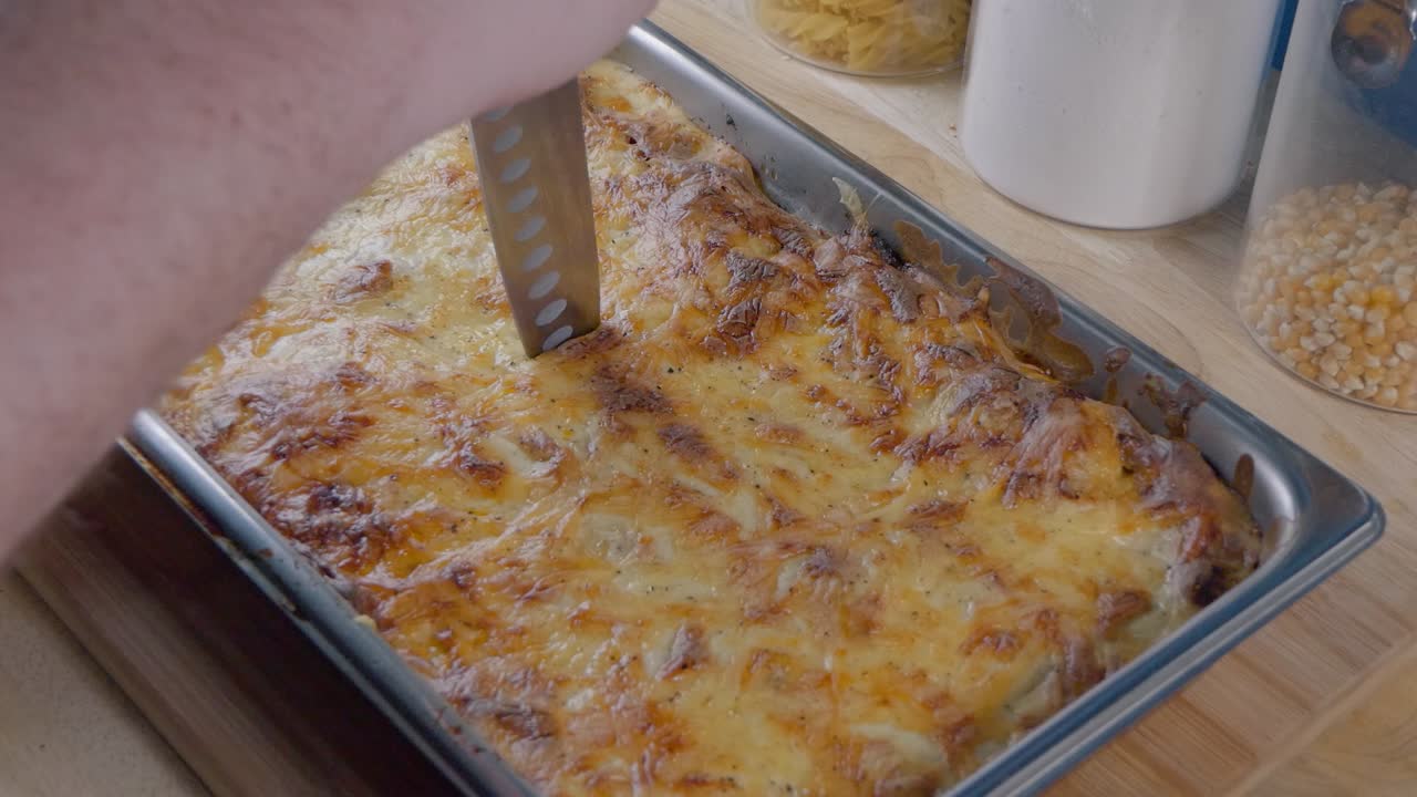 usando un cuchillo para cortar una lasagna recién cocinada en el mostrador de la cocina