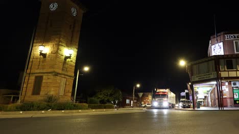 vehicles pass by a historic tower at night