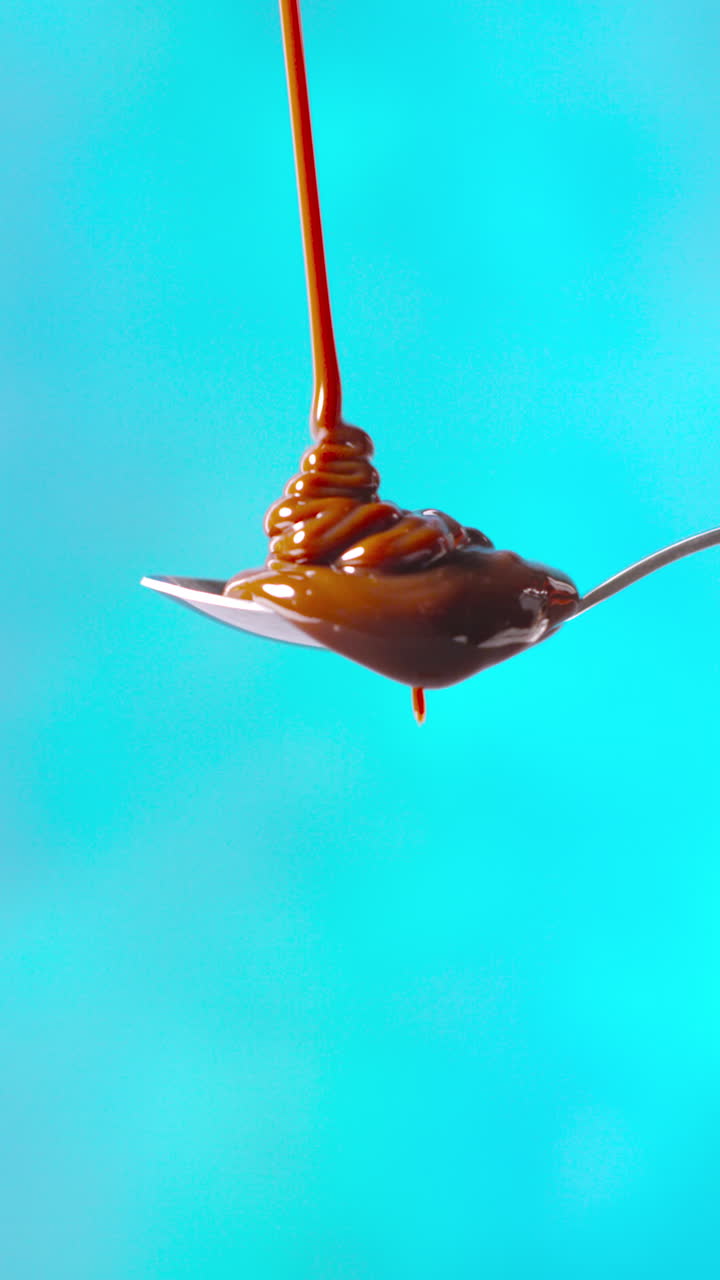 Vertical Video Of Melted Chocolate Being Poured Onto Spoon And Overflowing Against Blue Coloured Background With Copy Space